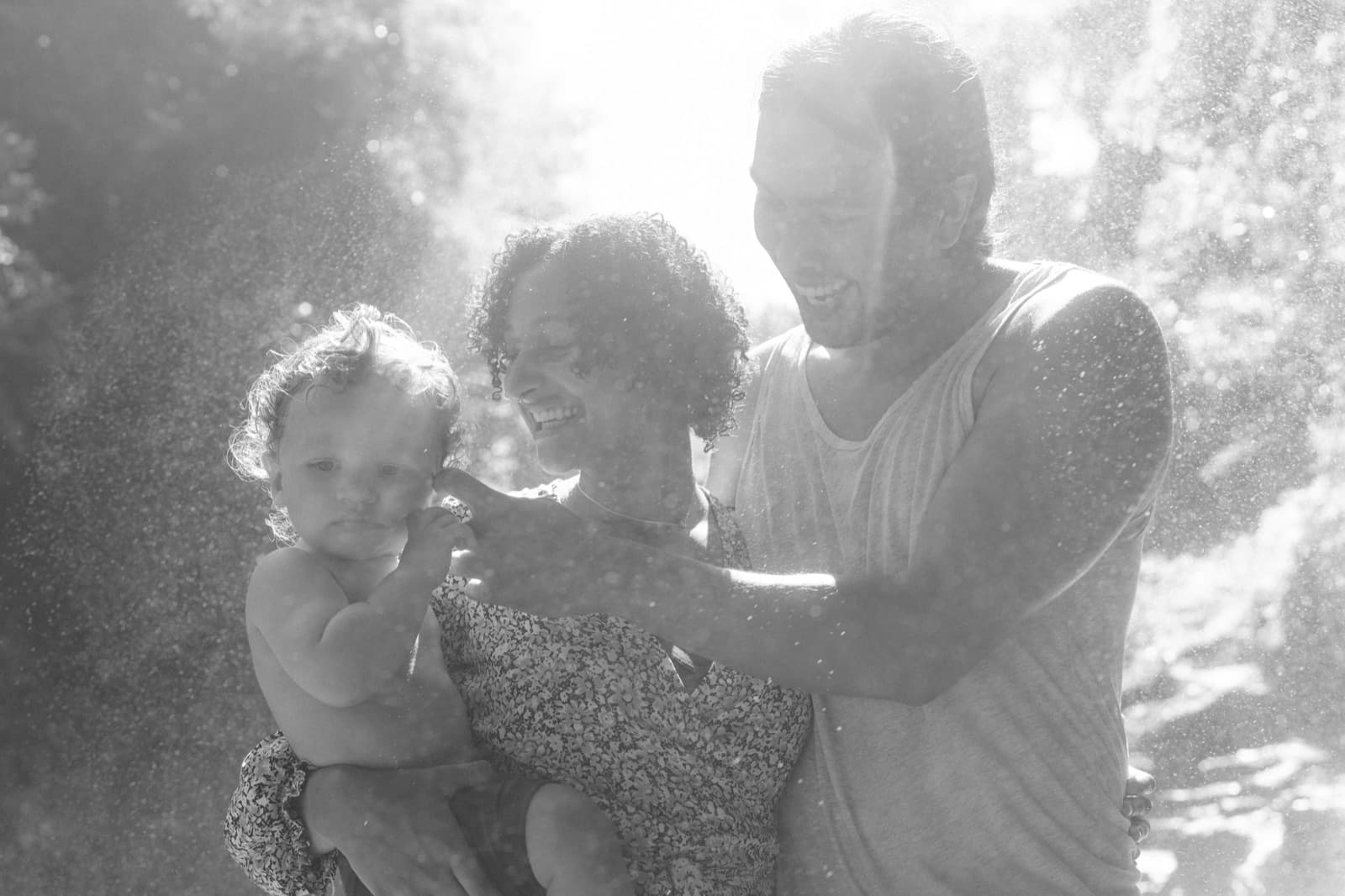 Three of us — Elli, John, and our toddler — sun-backed, water-spray around
