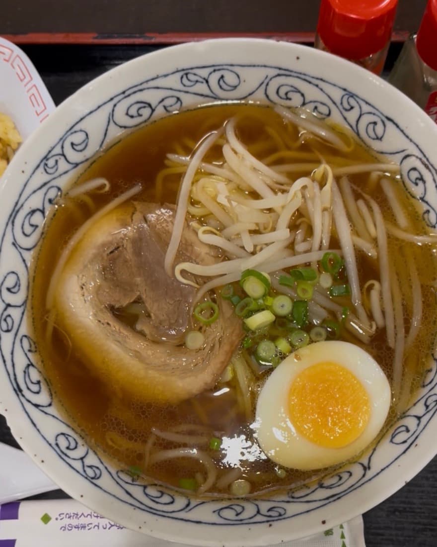 Shoyu ramen in a blue-patterned bowl — clear soy broth with noodles, bean sprouts, a slice of chashu pork, half a soft-boiled egg and scallion