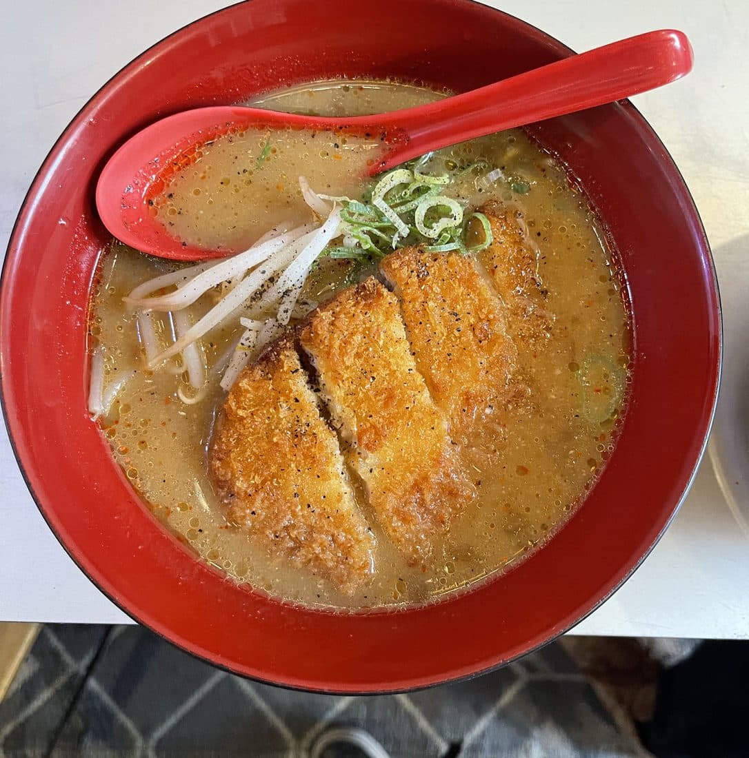 Curry ramen with crisp pork katsu slices, bean sprouts and green onion in a red bowl